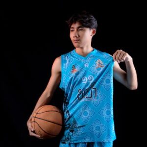 Young Asian basketball player in blue jersey posing in a studio with a black background.